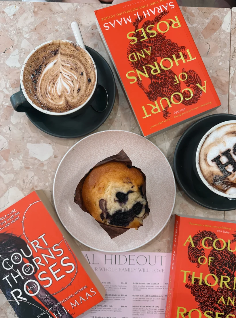 Book club au café : deux cafés, un muffin et trois exemplaires de A Court of Thorns and Roses sur une table en marbre